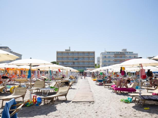 Plage bondée avec parasols et transats, bâtiments en arrière-plan.